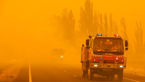 Fire burns in the grass along the road as firetrucks pass by near Bumbalong, south of the Australian capital, Canberra