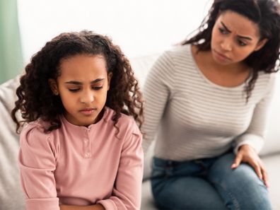Mother comforting pre-teen daughter sitting on couch