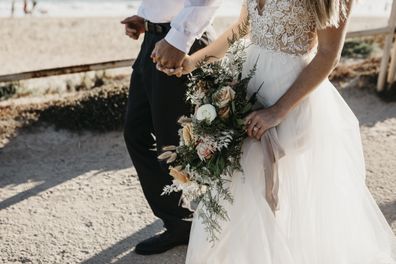 Close-up of bride and groom walking on path at the coast