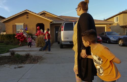 Neighbour Avery Sanchez, 6, peeks behinds his mother, Liza Tozier, outside the California home where people are placing gifts for the children. (AAP)