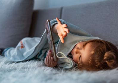 Toddler wrapped in blanket playing on iPad. 