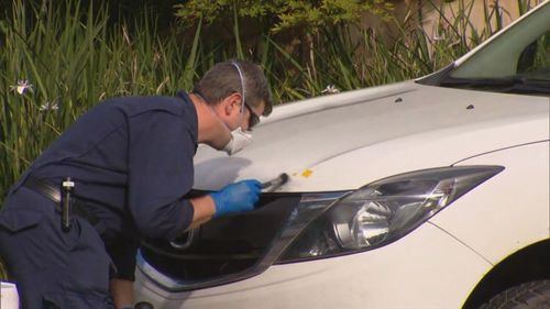 A police officer searches for evidence on a vehicle.