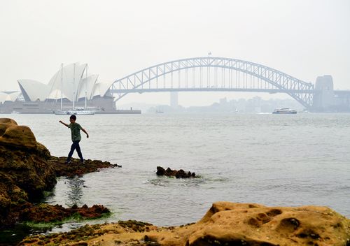 A young boy climbs on the rocks at Mrs Macquarie's Chair as smoke haze from bushfires in New South Wales blankets the CBD in Sydney