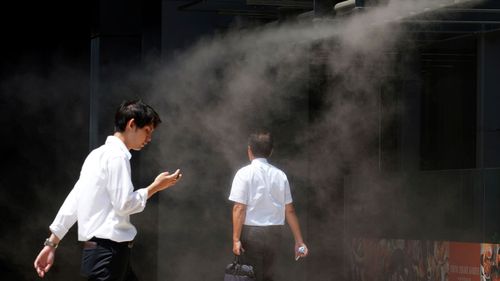 People cool down under a cooling mist spot at a building in Tokyo as temperatures soar above 35 degrees.