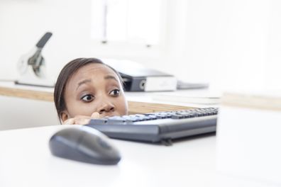 Woman afraid of boss. Woman ducking under office desk.