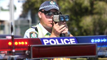A NSW police officer zeroes his speed camera on cars. The NSW government is considering ditching speed camera warning signs in a move that it claims could save lives.