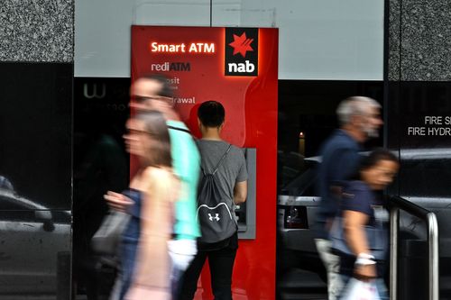 A man uses an NAB ATM arsenic pedestrians locomotion past.