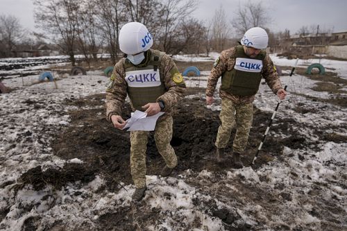 Members of the Joint Centre for Control and Coordination on ceasefire of the demarcation line, or JCCC, survey a crater from an artillery shell that landed near a school in Vrubivka, one of the at least eight that landed in the village today, according to local officials, in the Luhansk region, eastern Ukraine, Thursday, Feb. 17, 2022. U.S.  