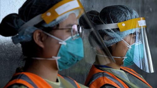 Health workers wearing full PPE wait for people to arrive for testing at a drive through coronavirus COVID-19 testing site in New South Wales.