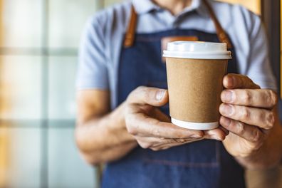 Photo of waiter holding and serving a paper cup of hot coffee