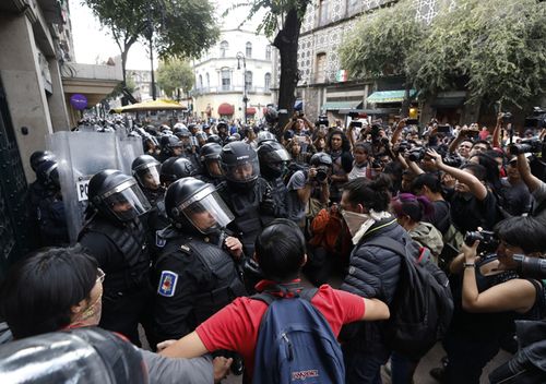 Mexico City police in riot gear are stopped by a handful of demonstrators and a circle of media, as they pursued masked protesters attacking businesses, during a largely peaceful protest for 43 missing teachers' college students, on the fifth anniversary of their disappearance. Groups of masked demonstrators flying anarchists flags and dressed in black attacked windows and defaced walls, on the tail end of the peaceful protest which was led by relatives and friends of the missing students.