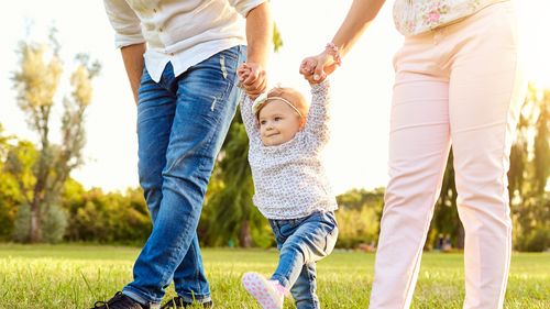 The first steps of the baby. Parents are teaching their child to walk. A happy family.