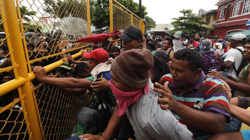 Central American migrants argue with police through a border crossing barrier at the Guatemalan town of Tecun Uman.