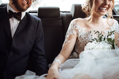 Newlywed bride and groom holding hands in the back seat of their wedding car