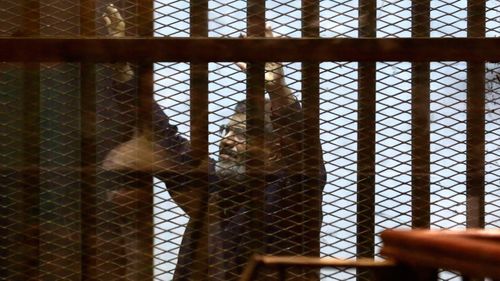 Morsi raises his hands inside a defendants cage in a makeshift courtroom at the national police academy in Cairo in 2015.