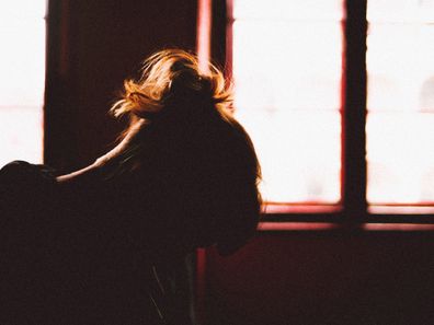 Woman in shadow sitting next to darkened window