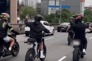 Group of young people riding e-bikes in Sydney peak hour traffic.