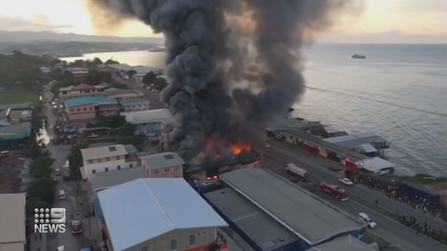 Thick smoke billows across properties in the Solomon Islands city as crowds fill the streets.