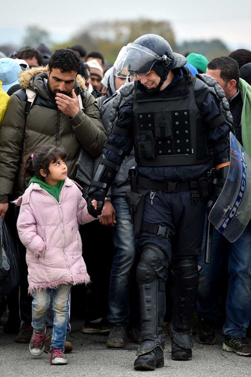 A police officer walks hand in hand with a young girl across Croatia's border with Slovenia. (Getty)