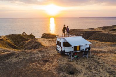 Couple on roof of camper van watching sunset.