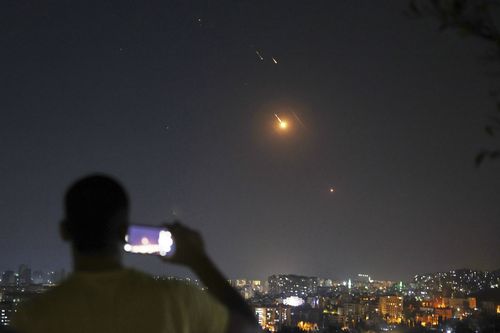 A man takes a cellphone photo as missiles fired from Iran toward Israel fly over Syrian territory in Damascus, Syria, early Wednesday, June 18, 2025. (AP Photo/Ghaith Alsayed)