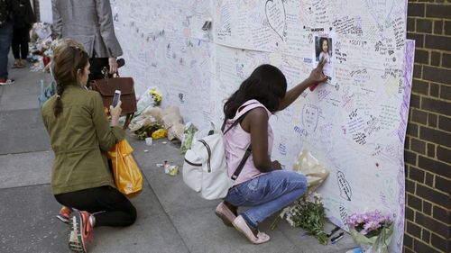 A woman touches a missing poster for 12-year-old Jessica Urbano on a tribute wall after laying flowers on the side of Latymer Community Church next to the fire-gutted Grenfell Tower in London. (AP)