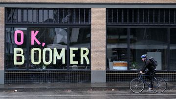 A man bikes past sticky notes arranged to display the phrase &quot;OK Boomer&quot; in a window of a business in Portland, Oregon.