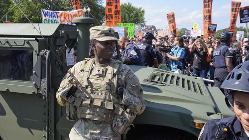 Washington Metropolitan Police officers and military police soldiers with the District of Columbia National Guard watch as activists protest President Donald Trump's federal takeover of policing of the District of Columbia.