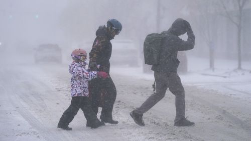 The Firestone family makes their way across Elmwood Avenue in Buffalo, N.Y. after stocking up on supplies at the grocery store, Friday, Dec. 23, 2022. Winter weather is blanketing the U.S. as a massive storm sent temperatures crashing and created whiteout conditions.(Derek Gee /The Buffalo News via AP)