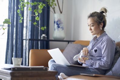 woman working from home using laptop computer eating snacks