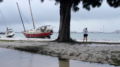 People walk past past boats on the beach in the aftermath of Tropical Storm Eta, Thursday, November12, 2020, in Gulfport, Florida. (AP Photo/Lynne Sladky)