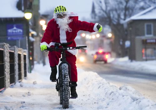 Брайан Дики, одетый как Санта-Клаус, поднимает большой палец вверх в знак благоговения байкеров, когда он едет на своем велосипеде по зимним улицам Карлтон-плейс, Онтарио, в канун Рождества, суббота, 24 декабря 2022 года. Крупная система зимних штормов продолжает действовать. так.  затронет восточный Онтарио.  (Шон Килпатрик/The Canadian Press через AP)