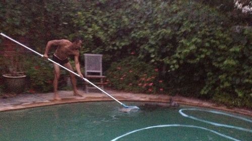 Mrs Nankivell's son-in-law shooing the marsupial out of the pool with a pool cleaning scoop. (Supplied)