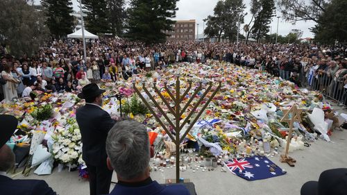 Rabino Motti Feldman, no canto inferior esquerdo, fala em uma cerimônia de acendimento da menorá em um memorial floral para as vítimas do tiroteio de domingo, no Pavilhão Bondi.