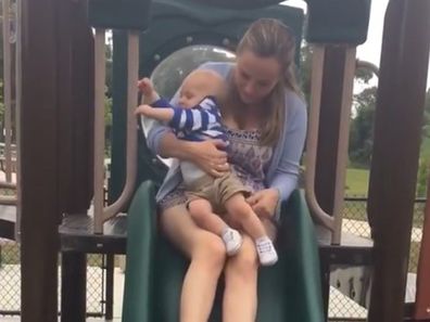 Mum riding down slide with baby in lap.