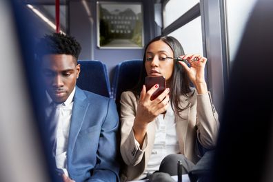 Businesswoman Sitting In Train Commuting To Work Putting On Make Up