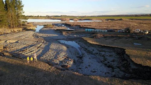 An aerial view of Arundel farm owner Andrew Milne with his children from left, Beau, 8, Taig, 7, and Gunnar, 5, on the edge of what used to be a small shingle pit until flooding gouged it out.