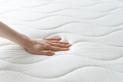 cropped shot of female hand testing new white orthopedic mattress on firmness in furniture store, memory foam surface, closeup