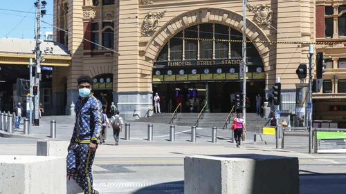 A man wearing a mask walks past Flinders Street Station in Melbourne.