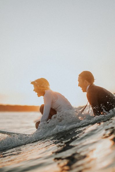 Australian bride and groom surf together before beach wedding