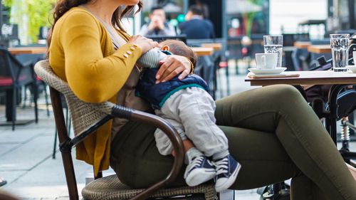 Young mother breastfeeding her baby boy in public while sitting in a cafe with her mother