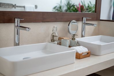 Close-up shot of clean bathroom sink with various toilet amenities on the bathroom counter of a luxurious villa. They provided the guests with drinking water, clean glasses, clean towels,  hand liquid soap and body cream in stone dispensers.