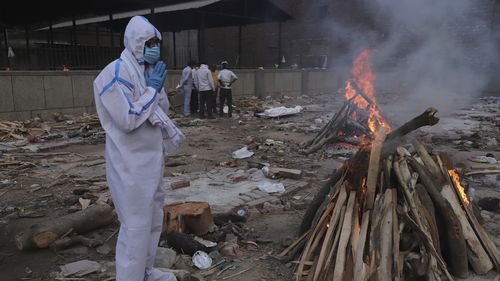 A man wearing personal protective equipment prays in front of the burning funeral pyre of his father who died of COVID-19, at a crematorium in New Delhi, India, Tuesday, May 11, 2021. (AP Photo/Amit Sharma)