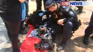 Police search the belongings of a woman thought to have brought a gas mask and a knife into the protest area. (9NEWS)