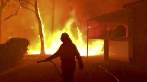 A firefighter sprays water on a fire moving closer to a home in Blackheath, New South Wales.