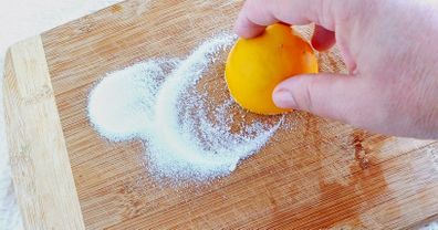 Woman's hand cleaning cutting board with lemon and salt