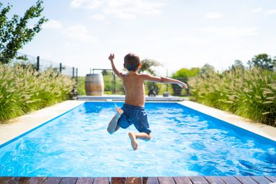 back view of 4 year old boy jumping into private pool - boy is unrecognizable so can be used anonymous summer fun series