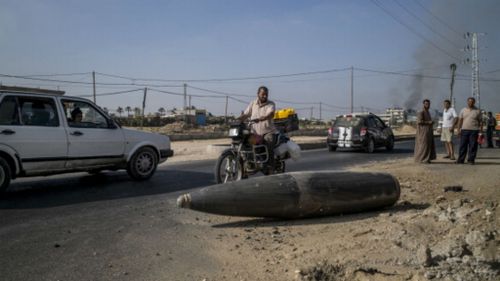 Palestinian onlookers and motorists pause to inspect an Israeli army bomb laying unexploded on the road, prior to the truce being broken. (Getty Images)