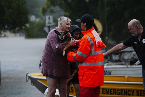 A NSW State Emergency Service (SES) volunteer assists a woman and her dog amid rising floodwaters.