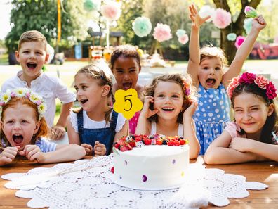 A portrait of children with cake standing around table on birthday party in garden in summer.